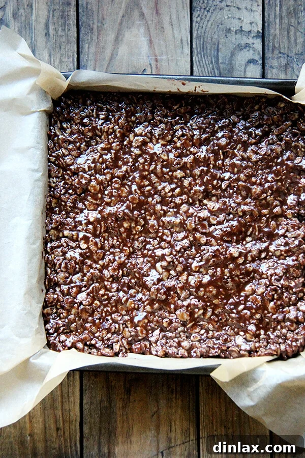 A close-up view of the crispy treat mixture, perfectly pressed and smoothed into the pan, demonstrating a neat and uniform base ready for the next layer.