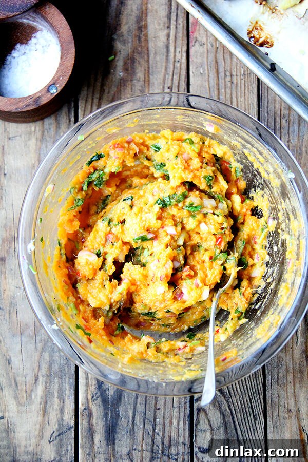 A vibrant bowl of mashed sweet potatoes, garnished with fresh green chilies, a wedge of lime, and aromatic cilantro leaves, resting on a rustic wooden surface. This dish offers a refreshing twist on classic sweet potato preparations, perfect as a healthy and flavorful side.