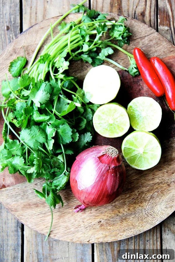 A cutting board adorned with fresh ingredients: bright green limes, fragrant cilantro sprigs, thinly sliced red onion or shallots, and vibrant red chilies, all prepped and ready for the recipe.
