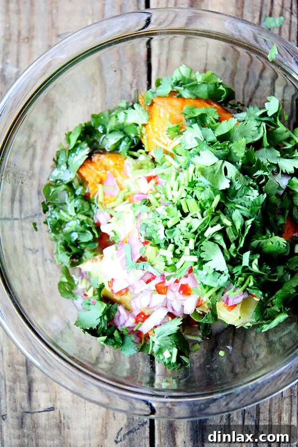 The process of combining flavors: chopped cilantro, macerated shallots, and chilies, along with fresh lime juice and olive oil, being added to a bowl of mashed sweet potatoes. This step creates the vibrant, guacamole-like texture and taste.