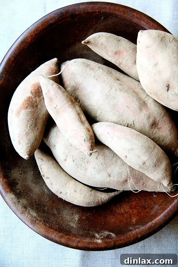 A rustic bowl filled with whole, unpeeled sweet potatoes, ready for preparation.