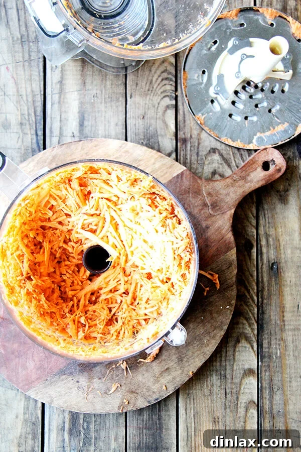 Finely grated sweet potatoes accumulating in the bowl of a food processor, showcasing the efficiency of the shredder attachment.