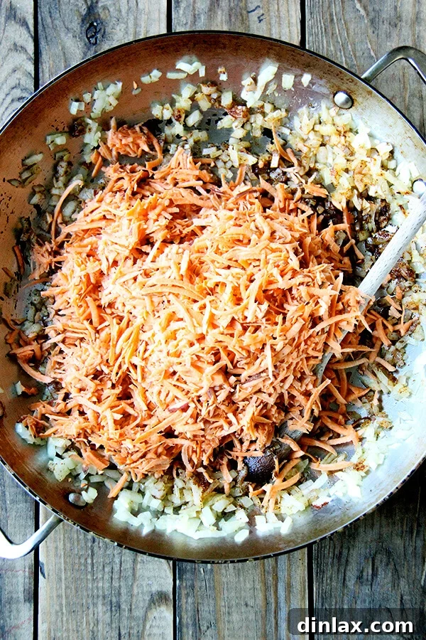 Grated sweet potatoes being added to a pan with sautéed onions and a colorful blend of cumin and chili powder, ready to be cooked into the quesadilla filling.