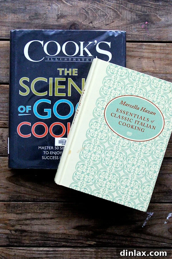 Two influential cookbooks, 'Essentials of Classic Italian Cooking' by Marcella Hazan and 'The Science of Good Cooking' by Cook's Illustrated, resting on a table.