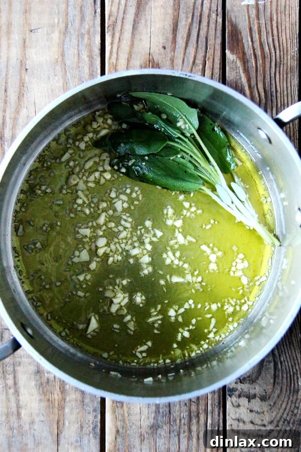 Minced garlic and fresh sage leaves gently sizzling in olive oil in a saucepan, creating an aromatic base for the beans.