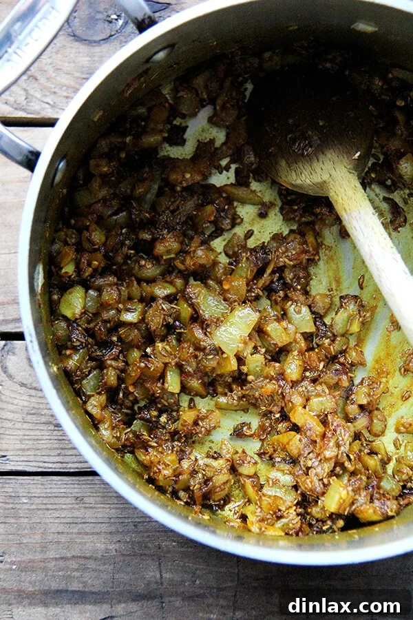 Close-up shot of translucent, softened onions mingling with the toasted spices in a pot. The aromatic foundation for the dal is clearly visible, with the spices releasing their fragrance into the sweet onions before the lentils are added.