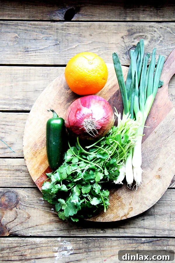 A cutting board filled with freshly prepared ingredients for white bean salsa: cilantro, red onion, orange segments, scallions, and jalapeño.