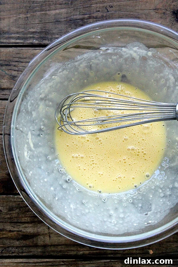 The remaining four eggs being whisked into the flour and egg mixture, creating a smooth base.