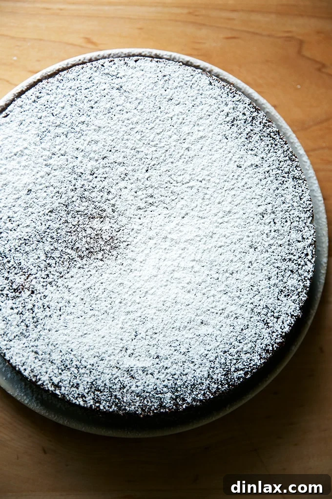 A whole orange and olive oil cake, lightly dusted with powdered sugar, ready to be sliced.