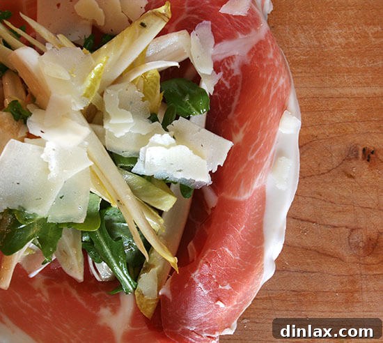 An overhead shot of a vibrant prosciutto, pear, and endive salad, beautifully arranged.