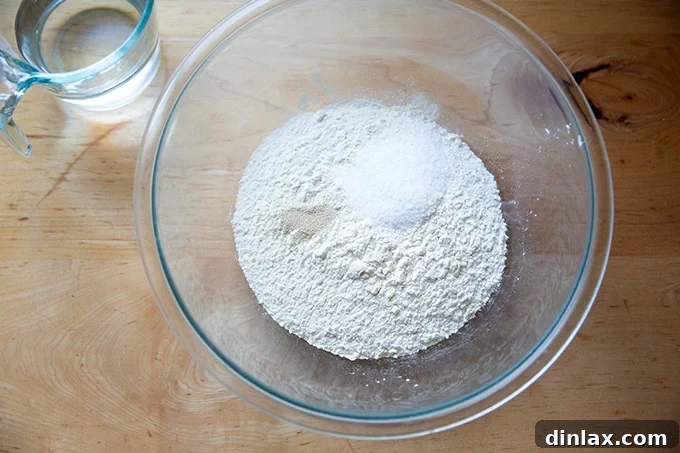 A large glass bowl containing a perfectly measured mixture of flour, salt, and instant yeast, ready for the addition of water.