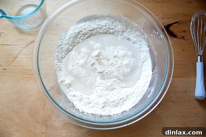 Clear water being poured into a large glass bowl, beginning the mixing process for the no-knead bread dough.