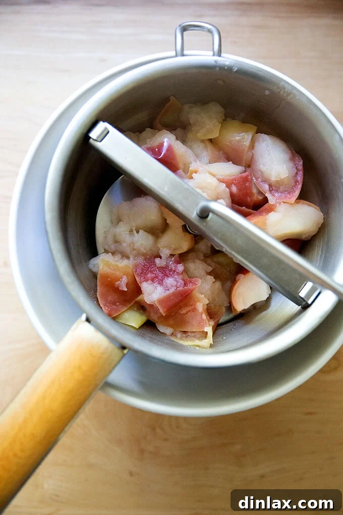 Warm Spiced Applesauce 8 A food mill actively processing cooked apples over a large mixing bowl, separating the smooth applesauce from the skins.