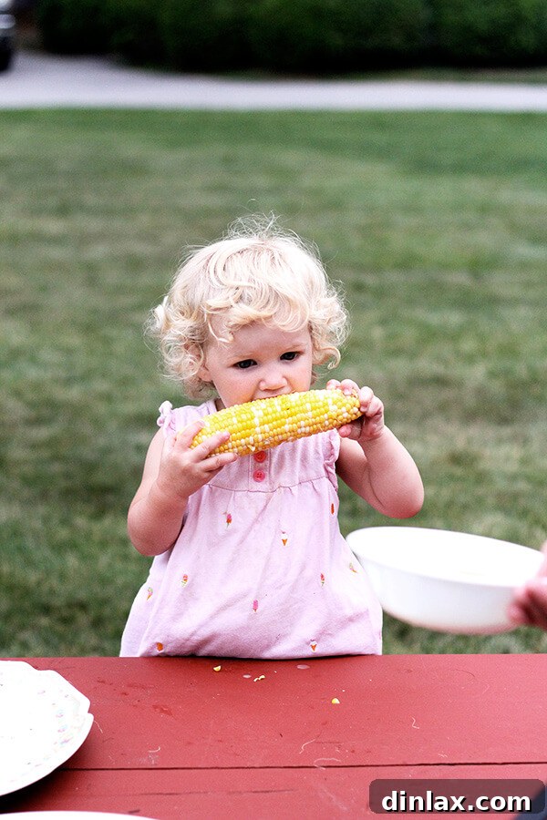 The Queen of American Lakes 11 Baby Tig happily discovering and eating corn on the cob, a delightful and messy first-time experience captured perfectly.