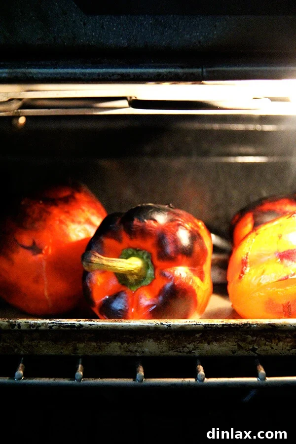 Red bell peppers roasting in an oven on a sheet pan, blistering and charring to perfection for delicious wraps.
