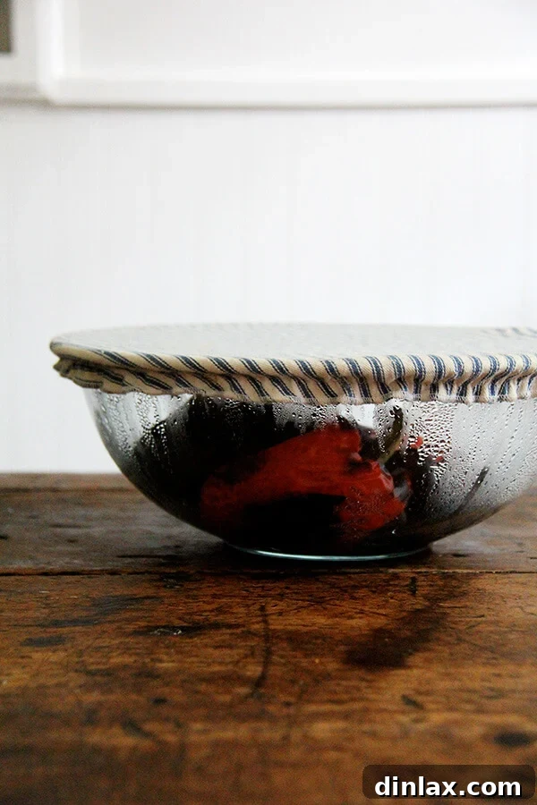 Steaming roasted red peppers in a bowl covered with plastic wrap to loosen their skins for easy peeling.