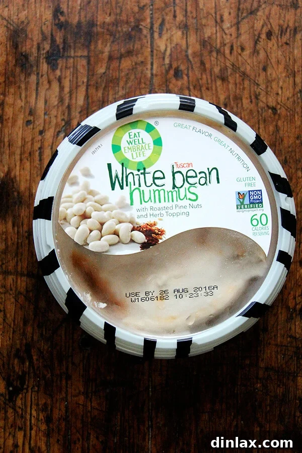 A container of 'Eat Well Embrace Life' white bean hummus, perfect for healthy and delicious wraps.