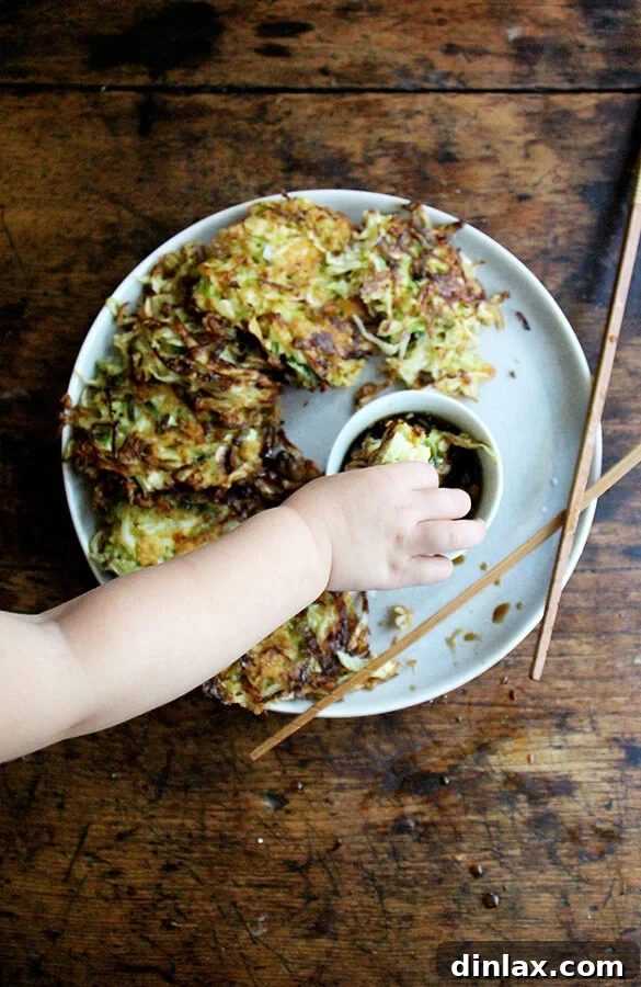 Overhead shot of a child dipping a piece of Okonomiyaki, a Japanese cabbage pancake, into a small bowl of soy dipping sauce.