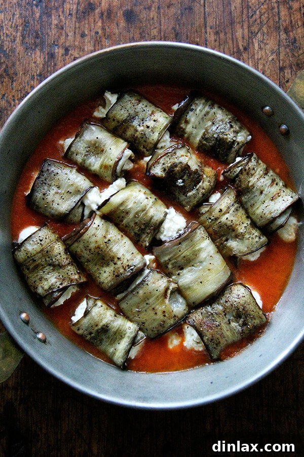 Eggplant involtini arranged in a baking dish, covered with vibrant tomato sauce, ready for the oven.