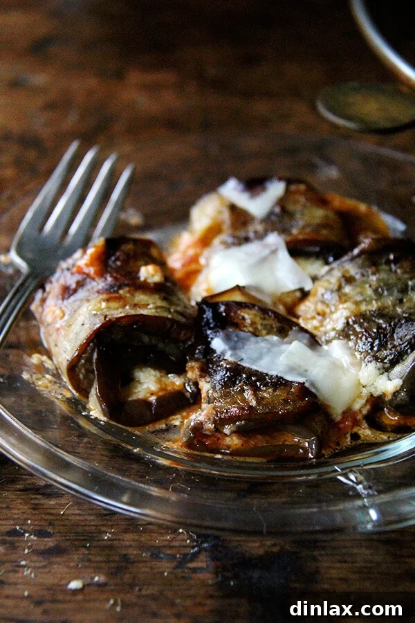 A single serving of eggplant involtini on a white plate, with a fork, ready to be enjoyed.