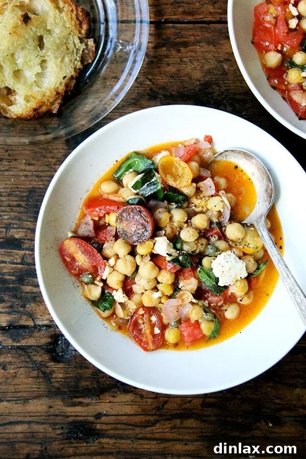 These stewy chickpeas are a mix of chickpeas, tomatoes, basil, and feta. After I made it the first time, we devoured most if it immediately with crusty, olive oil-toasted bread, then snacked on the leftovers for days. // alexandracooks.com A vibrant bowl of stewy chickpeas, fresh tomatoes, and creamy feta, garnished with basil – a perfect late-summer delight.