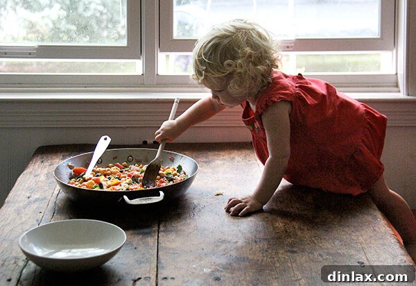Mediterranean Chickpea and Tomato Stew with Feta 5 A charming scene of a toddler, Tig, intently stirring the stewy chickpeas on a table, adding a personal touch to the cooking process.