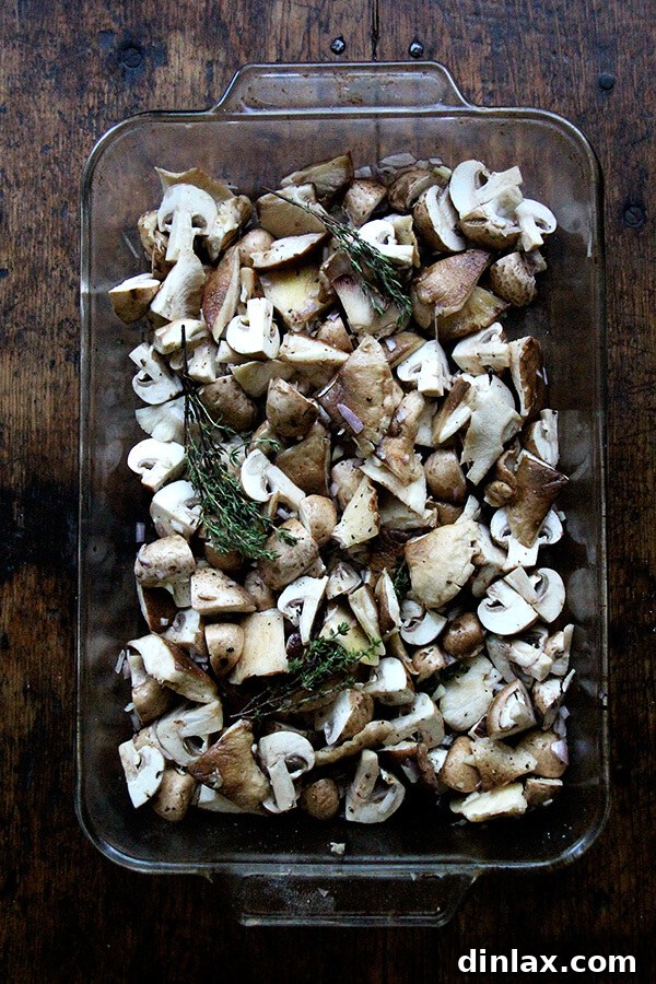 A 9x13-inch baking pan filled with quartered mushrooms, sprigs of fresh thyme, chopped shallots, minced garlic, and a splash of sherry, ready for the oven.