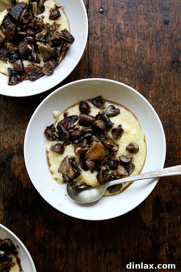 Two cozy bowls of creamy polenta topped with generous servings of rich, roasted mushrooms and drizzled with their savory pan sauce, garnished with fresh herbs.