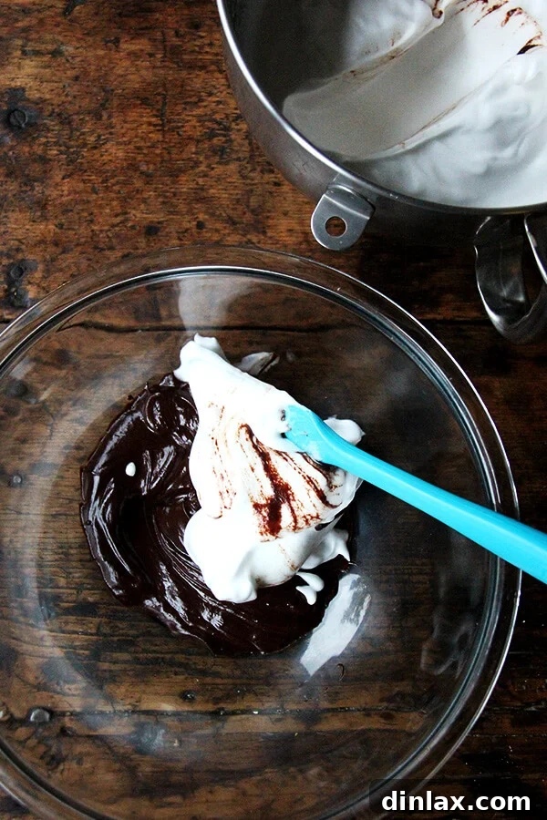 A spatula gently folding the ethereal whipped aquafaba into a rich, melted chocolate mixture, creating a marbling effect.