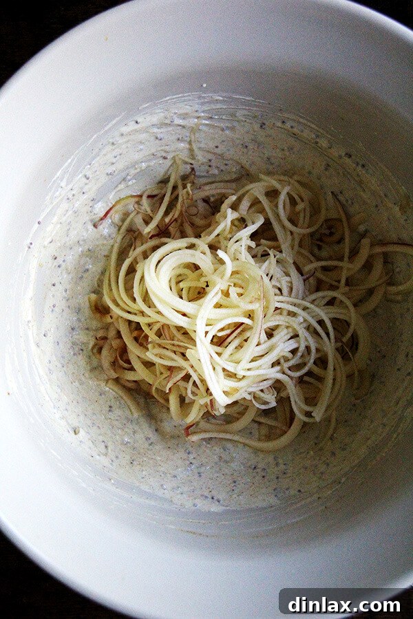 The process of tossing freshly spiralized apples with the vibrant curried yogurt dressing, ensuring every piece is coated with flavor.