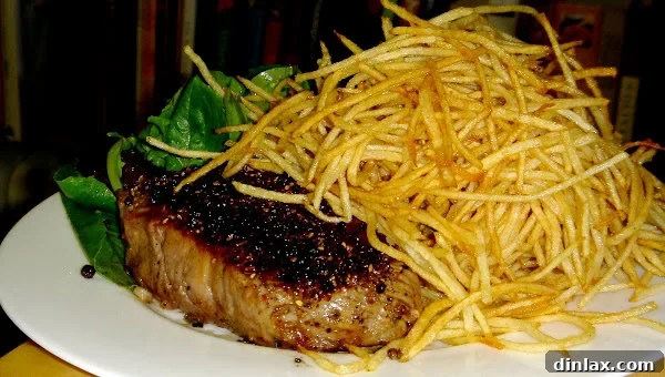 Perfectly seared New York Strip Steak served alongside golden, crispy French fries, with a small bowl of spicy aioli on the side, ready to be enjoyed.
