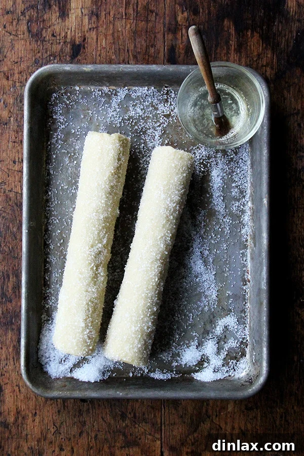 Dorie Greenspan's Classic Vanilla Bean Sablés 12 Two logs of sablé cookie dough, beautifully rolled in decorative sparkling sugar, positioned on a small sheet pan ready for slicing and baking.
