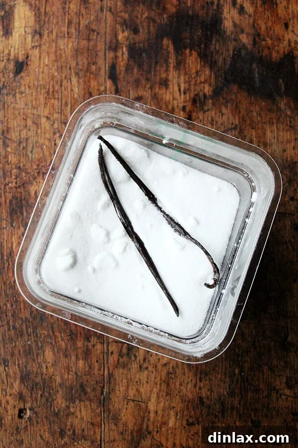 Dorie Greenspan's Classic Vanilla Bean Sablés 4 A large, clear container of granulated sugar with two used vanilla bean pods tucked inside, demonstrating how to make vanilla sugar.