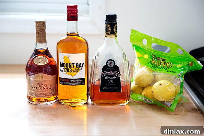 A selection of high-quality ingredients, including brandy, cognac, rum, lemons, and sugar, for Philadelphia Fish House Punch, neatly arranged on a kitchen countertop.