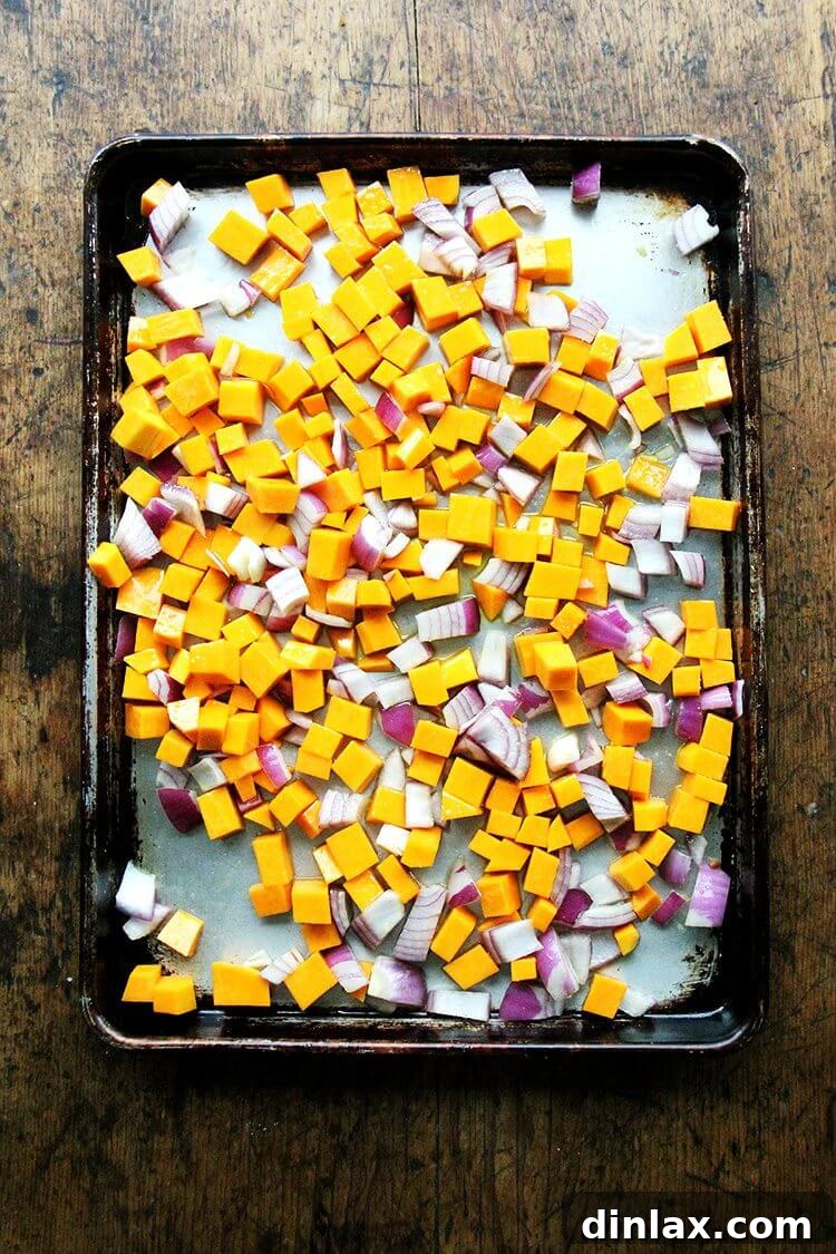 A sheet pan filled with perfectly cubed butternut squash and uniformly diced red onion, seasoned and ready for roasting, showcasing the initial prep step for the quinoa bake.