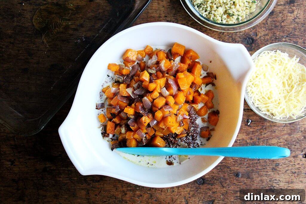 A large mixing bowl containing fluffy cooked quinoa, perfectly roasted butternut squash and onions, and a splash of milk, ready for the next stage of combining ingredients for the bake.