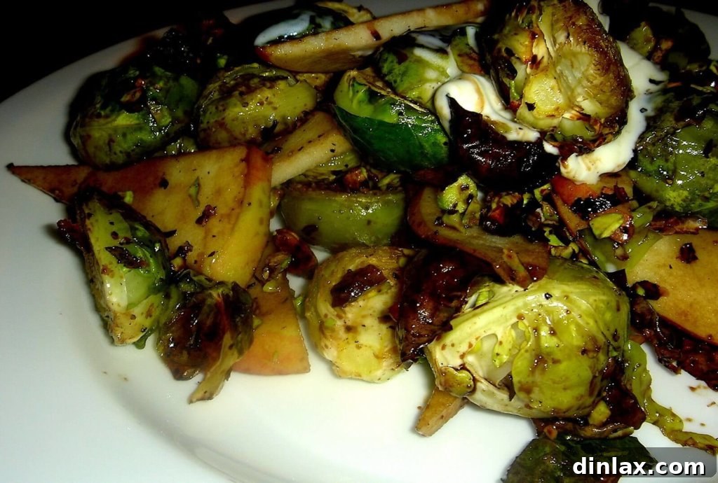 Up-close shot of beautifully roasted Brussels sprouts mixed with apple slices, crème fraîche, and pistachios, drizzled with balsamic glaze. A vibrant and appealing side dish.