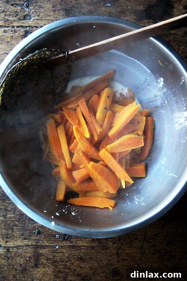 Par-boiled sweet potato wedges being added to the cornstarch slurry in a bowl.