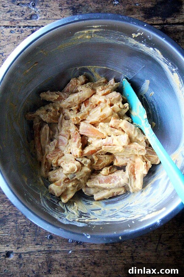 Sweet potato wedges thoroughly coated in a light orange, starchy paste, ready for frying.
