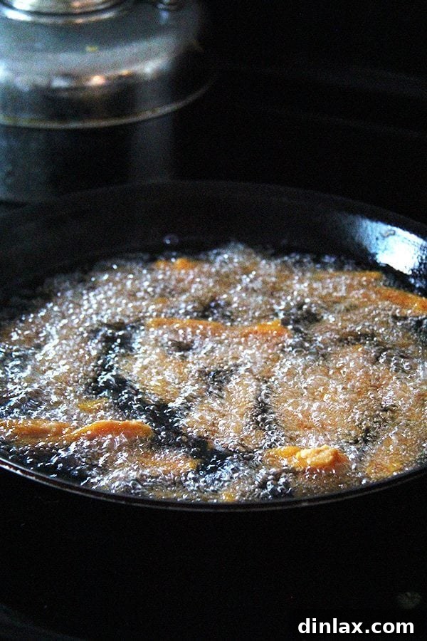 Thick-cut sweet potato fries sizzling in hot oil during the frying process.
