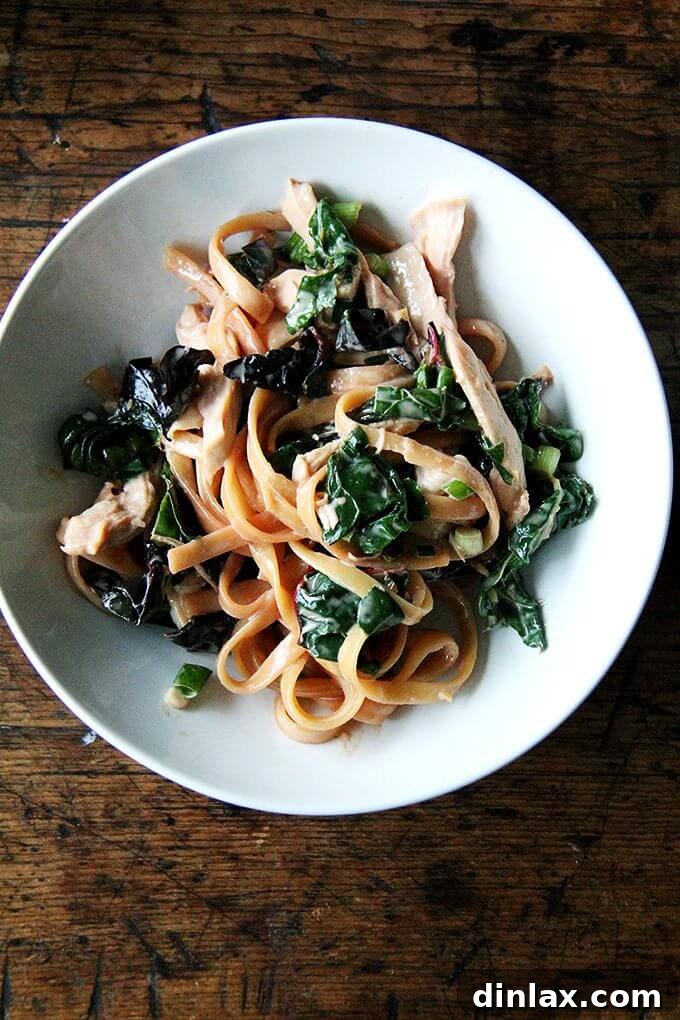 A vibrant bowl of sesame noodles with shredded chicken and sautéed Swiss chard, garnished with scallions.