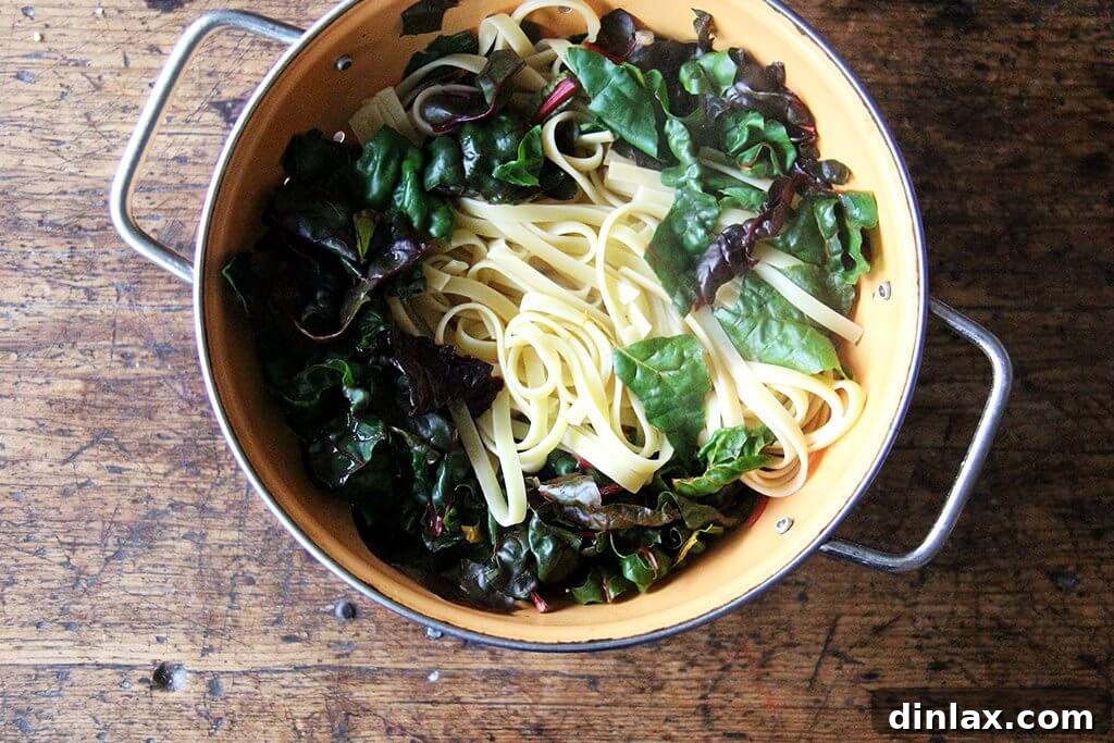 Drained fettuccine noodles resting over a bed of fresh Swiss chard in a colander.