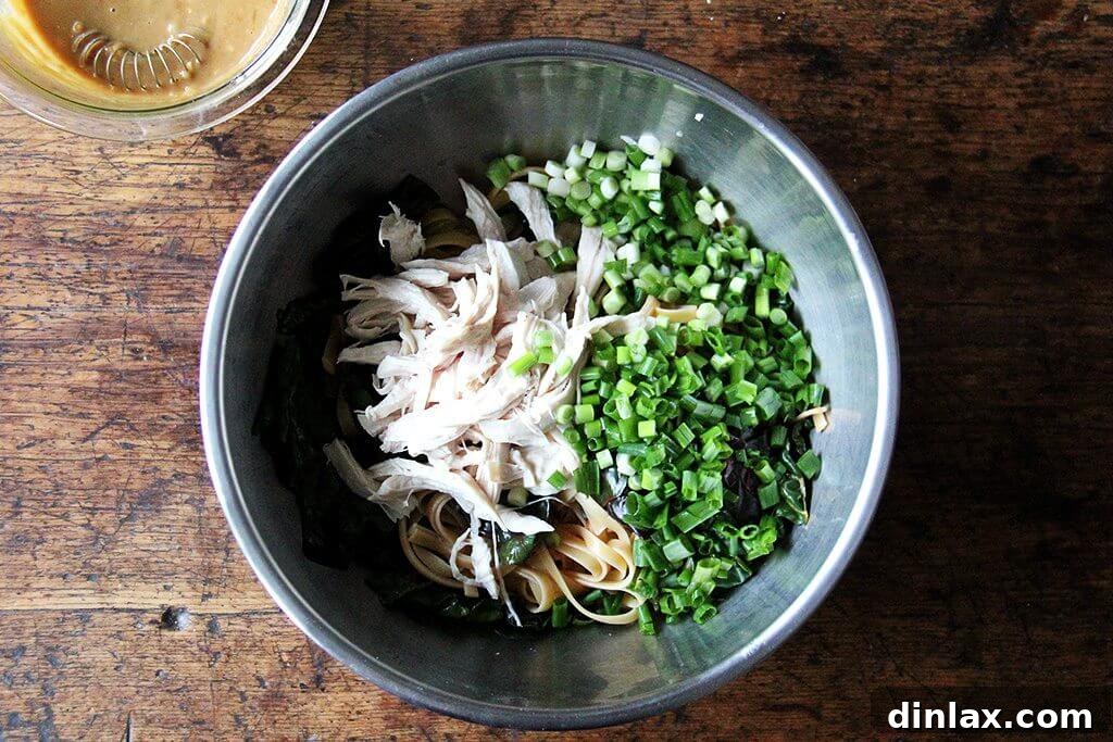 Shredded chicken and sliced scallions being added to a bowl of noodles and chard.
