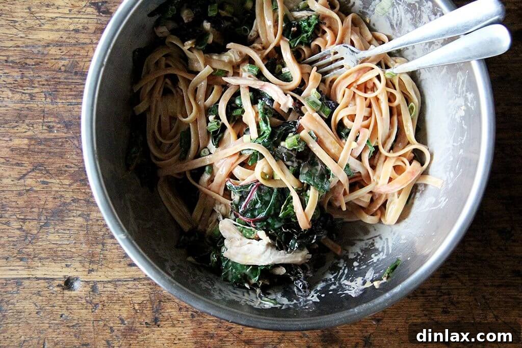 A chef's hands tossing the sesame noodles, chicken, and chard with the dressing in a large bowl.