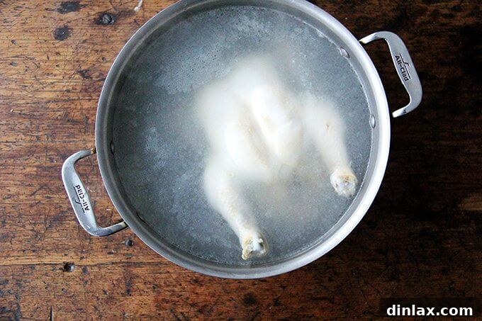 Asian-Inspired Sesame Almond Chicken Slaw 4 A whole chicken gently poaching in a large pot of simmering water on the stovetop, ensuring tender and flavorful meat for the salad.