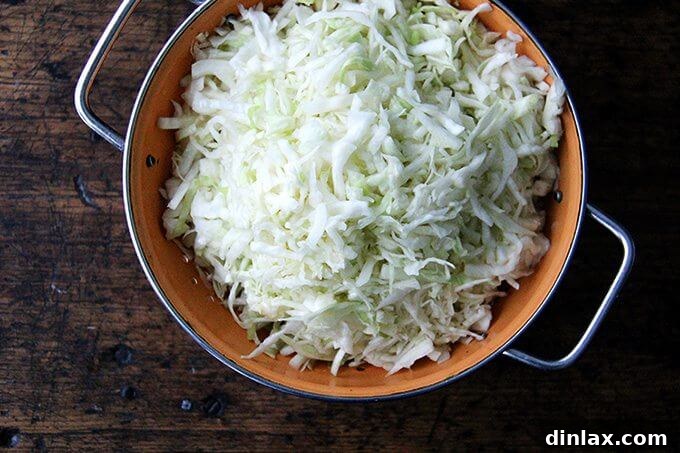 Asian-Inspired Sesame Almond Chicken Slaw 5 Close-up view of shredded cabbage draining thoroughly in a large colander after being salted and rinsed, ready for dressing.