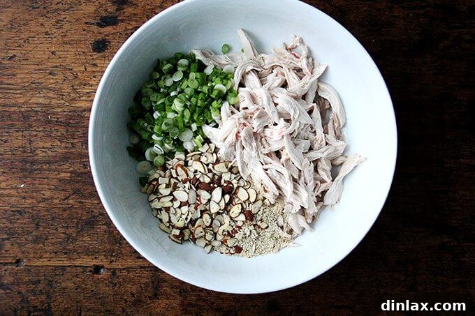 Asian-Inspired Sesame Almond Chicken Slaw 7 Various components of the chicken and cabbage salad, including shredded chicken, cabbage, and dressing, beautifully arranged in a large mixing bowl before tossing.