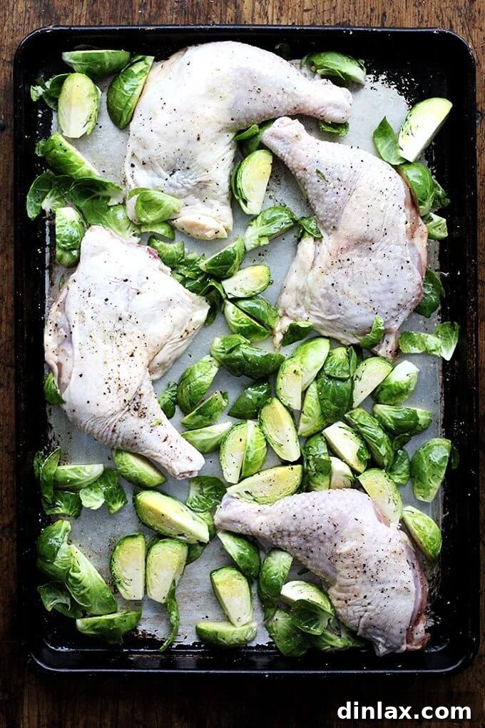 Sheet Pan Balsamic Chicken and Roasted Brussels Sprouts 2 A sheet pan with raw chicken legs and halved Brussels sprouts, seasoned and ready for roasting.