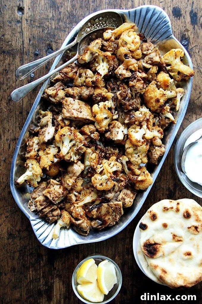 A vibrant platter of sheet pan chicken and cauliflower shawarma, garnished with fresh herbs and lemon wedges.