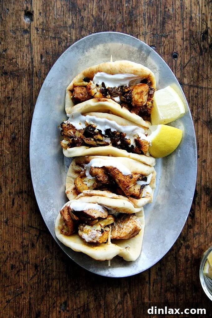 A sizzling platter presenting sheet pan chicken and cauliflower shawarma nestled in mini pita breads, ready for serving.